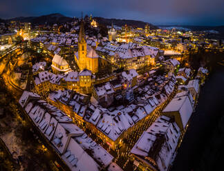 Aerial view of snow-capped roofs of historic town of Baden, Switzerland, with colorful christmas lights lighting the streets - AAEF08413