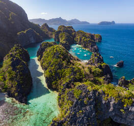 Aerial view of the famous big lagoon with outrigger boats in the blue and turquoise water. Some more islands in the background. El Nido, Palawan, Philippines. - AAEF08609