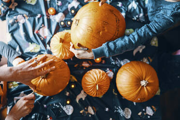 Overhead view of pumpkins on a table with hands cutting or drawing on them. - CUF55072