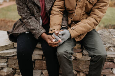 Zwei Menschen halten sich an den Händen, eine schwarze Frau und ein weißer Mann, die an einer Wand sitzen. - ISF24035