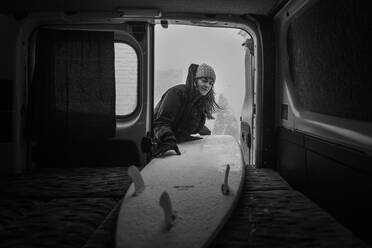 Frau, die ein Surfbrett in den Kofferraum eines Wohnmobils packt. Wintersurfen - ISF24046