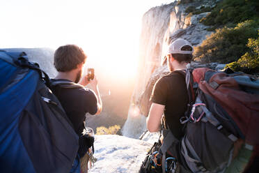 Rear view of two men taking pictures of rocks and a sunset with a mobile phone. - ISF24099