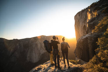 A group of people standing on a rock photographing a sunset. - ISF24101