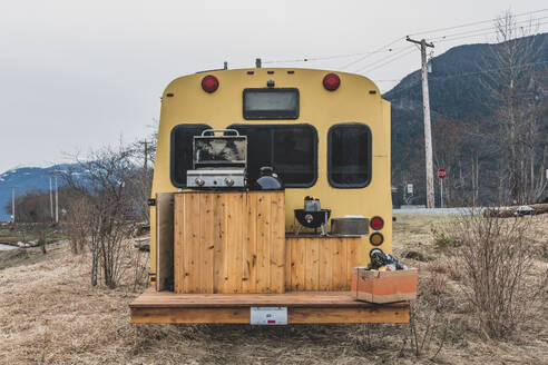 Rückansicht eines Wohnmobils mit einem Holzdeck, das für einen Grillabend in einer winterlichen ländlichen Landschaft aufgestellt ist. - ISF24120