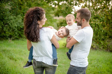 Porträt einer Familie mit zwei Kindern, die auf einer Wiese stehen, lächeln und sich umarmen. - ISF24154