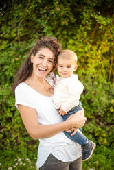 Porträt einer Frau, die einen kleinen Jungen hält, der auf einer Wiese steht und in die Kamera lächelt. - ISF24158