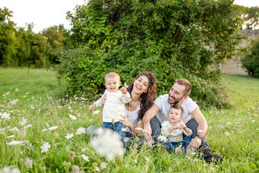 Porträt einer Familie mit zwei Kindern, die auf einer Wiese sitzen und in die Kamera lächeln. - ISF24160