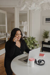 Woman with long dark hair sitting at dining table, looking at laptop computer. - ISF24162