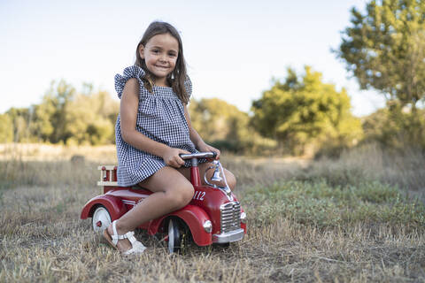 Portrait of smiling little girl with pedal car in nature stock photo