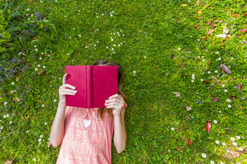 Girl lying on meadow reading a book, top view stock photo