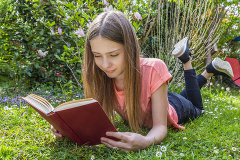 Mädchen liegt auf einer Wiese und liest ein Buch, lizenzfreies Stockfoto