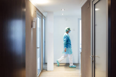 Mature male dentist walking in illuminated hallway at medical clinic - JCMF00727
