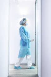 Mature female dentist walking in illuminated hallway - JCMF00729
