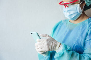 Mature female dentist using mobile phone while standing against white wall at clinic - JCMF00731