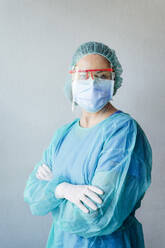 Confident female dentist wearing protective medical scrubs while standing with arms crossed against wall at clinic - JCMF00737