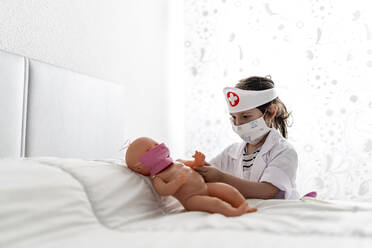 Mädchen im Arztkostüm, das seine Puppe mit einer Maske pflegt - EGAF00096