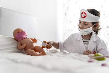 Mädchen im Arztkostüm, das seine Puppe mit einer Maske pflegt - EGAF00102