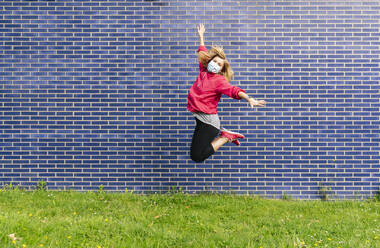 Frau mit chirurgischer Maske springt vor einer blauen Wand - DGOF01001