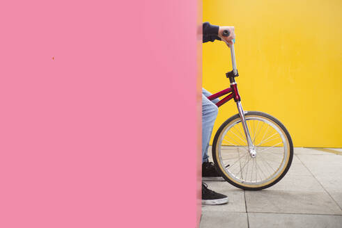 Teenage boy on BMX bike hiding behind pink wall - JCMF00743