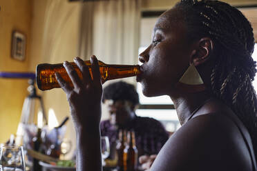 Nahaufnahme einer jungen Frau, die Bier aus einer Flasche trinkt, während sie zu Hause zu Mittag isst - VEGF02211