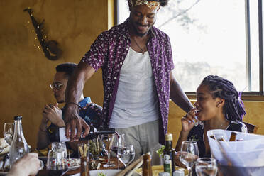 Smiling man serving wine for friends sitting at dining table - VEGF02219