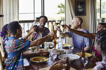 Smiling friends toasting drinks while sitting at dining table during lunch - VEGF02220