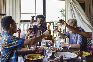 Smiling male and female friends toasting drinks while sitting at dining table during lunch - VEGF02221