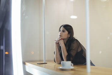 Thoughtful young woman sitting at illuminated coffee shop - OCAF00473