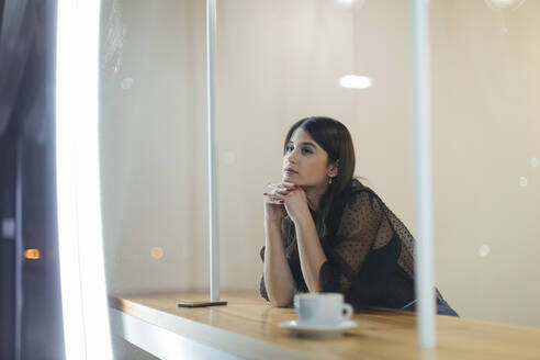 Nachdenkliche junge Frau sitzt in einem beleuchteten Café - OCAF00473