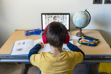 Rear view of boy listening to teacher through video call at home during pandemic outbreak - MGIF00949