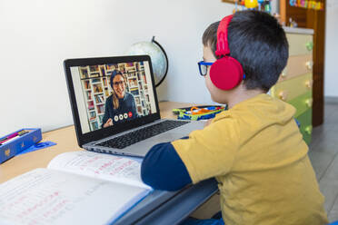 Boy listening to teacher through headphones during video call at home - MGIF00953