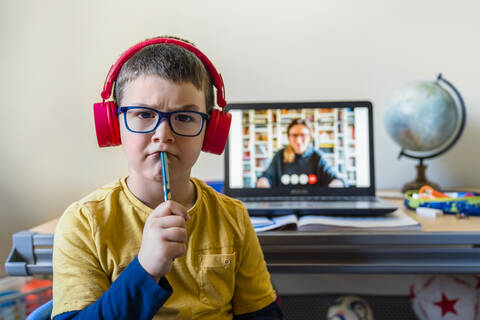 Nachdenklicher Junge sitzt während eines Videoanrufs zu Hause am Laptop, lizenzfreies Stockfoto