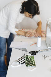 Homemade protective face masks on table by woman working at home - MRAF00514