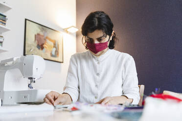 Selbstbewusste Frau, die während des Coronavirus eine selbstgemachte Gesichtsmaske anfertigt - MRAF00520