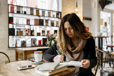 Woman writing in notebook in coffee shop - MGOF04248