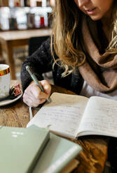 Woman writing in notebook in coffee shop - MGOF04249