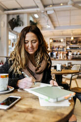 Frau schreibt in einem Café in ein Notizbuch - MGOF04250