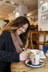 Woman writing in notebook in coffee shop - MGOF04251