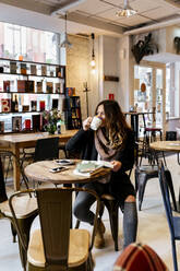 Woman drinking coffee in coffee shop - MGOF04252