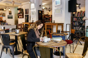 Frau schreibt in einem Café in ein Notizbuch - MGOF04253