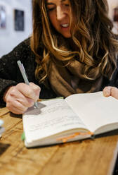 Woman writing in notebook in coffee shop - MGOF04265