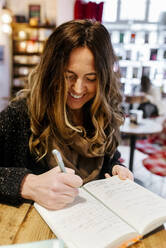 Woman writing in notebook in coffee shop - MGOF04266