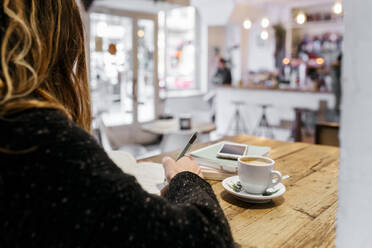 Frau schreibt in einem Café in ein Notizbuch - MGOF04267