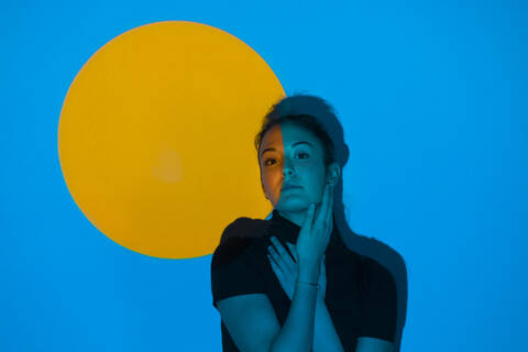 Junge Frau bewegt sich in blauem Licht vor einem gelben Kreis, lizenzfreies Stockfoto
