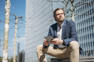 Businessman sitting on bench in the city holding tablet - JOSEF00559