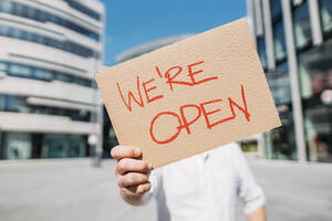 Shopkeeper holding cardboard with opening announcement in the city - JOSEF00562