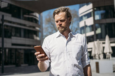 Geschäftsmann überprüft Smartphone in der Stadt - JOSEF00567