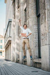 Excited shopkeeper holding cardboard with opening announcement in the city - JOSEF00573