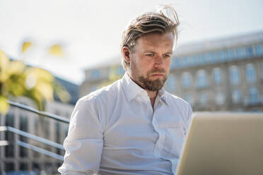 Businessman using laptop in the city - JOSEF00577