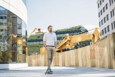 Businessman riding skateboard at construction site in the city - JOSEF00579